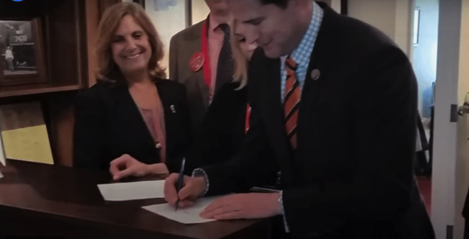 Seth Moulton, with Nancy Frates looking on, signs the first version of the ALS Disability Insurance Access Act at the May 2016 ALS Advocacy Conference